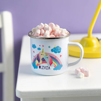 Mug with unicorn and rainbow design filled with marshmallows on a white surface.
